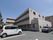マンション風の３階建ての施設。周りは駐車場になっており、付近は戸建住宅がある。２、３階の居室にはベランダがついている。