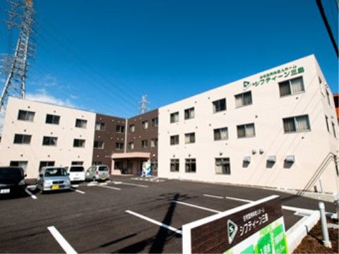 白と茶色の外壁が特徴の３階建ての建物である。駐車場が広く、20台以上車を停めることができるため、来訪者様は車でお越しいただける。