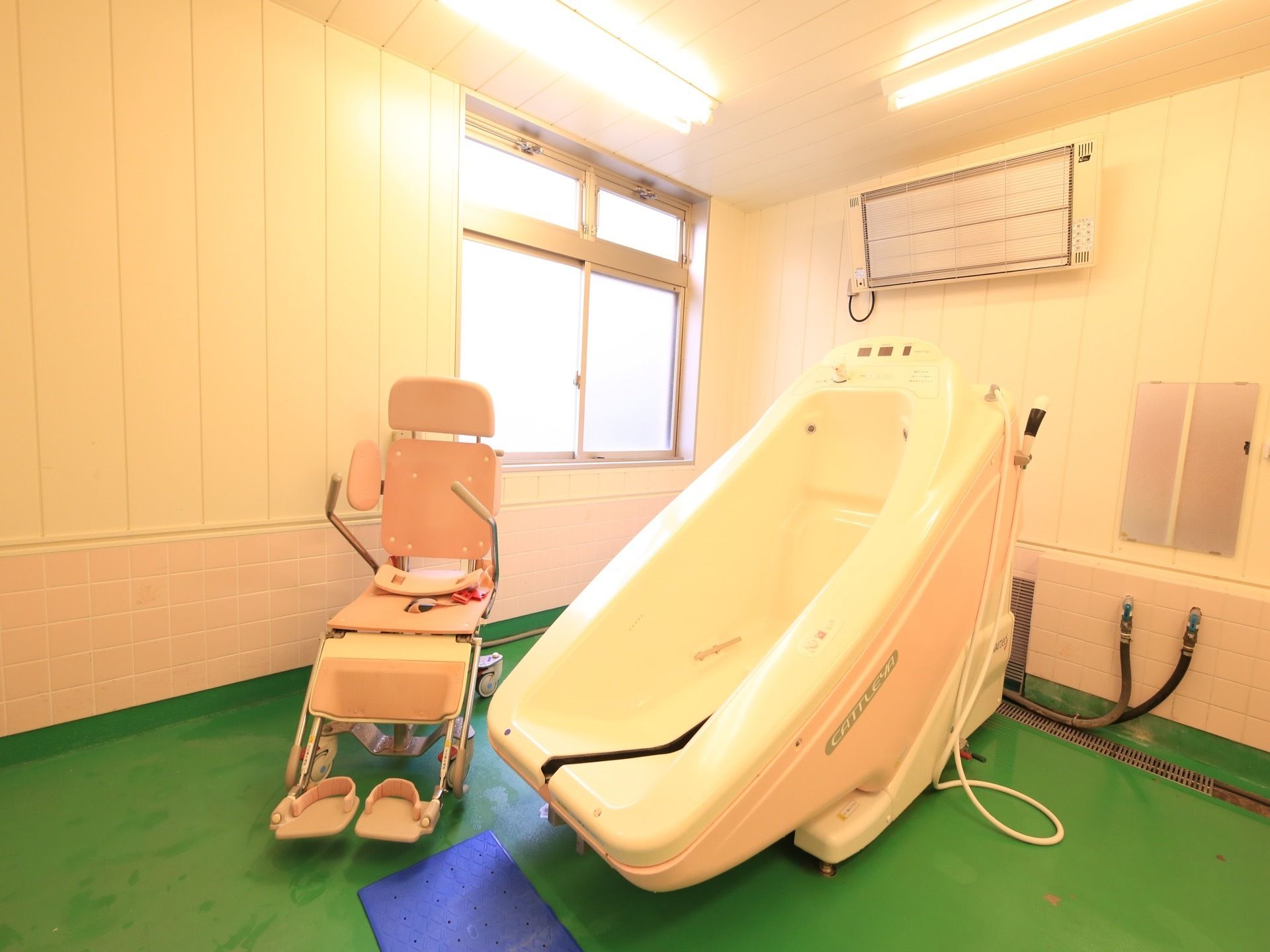 明るく広い介護浴室には、専用シャワーキャリーが備わった機械浴槽が設置されている。壁には、遠赤外線ヒーターが取りつけられている。