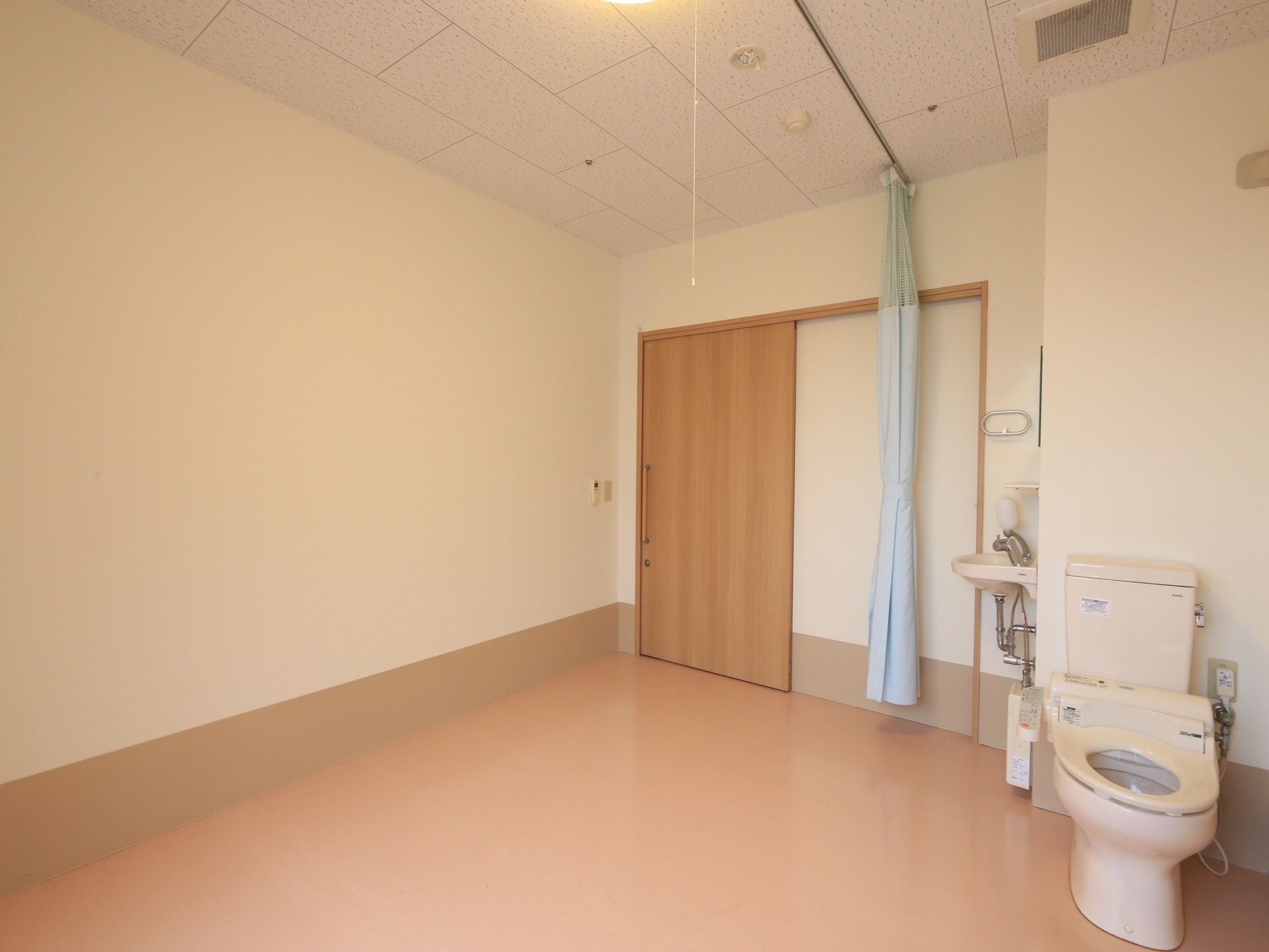 居室は広めの間取りになっている。トイレや洗面台が完備されており、仕切り用のカーテンが天井に取りつけられている。