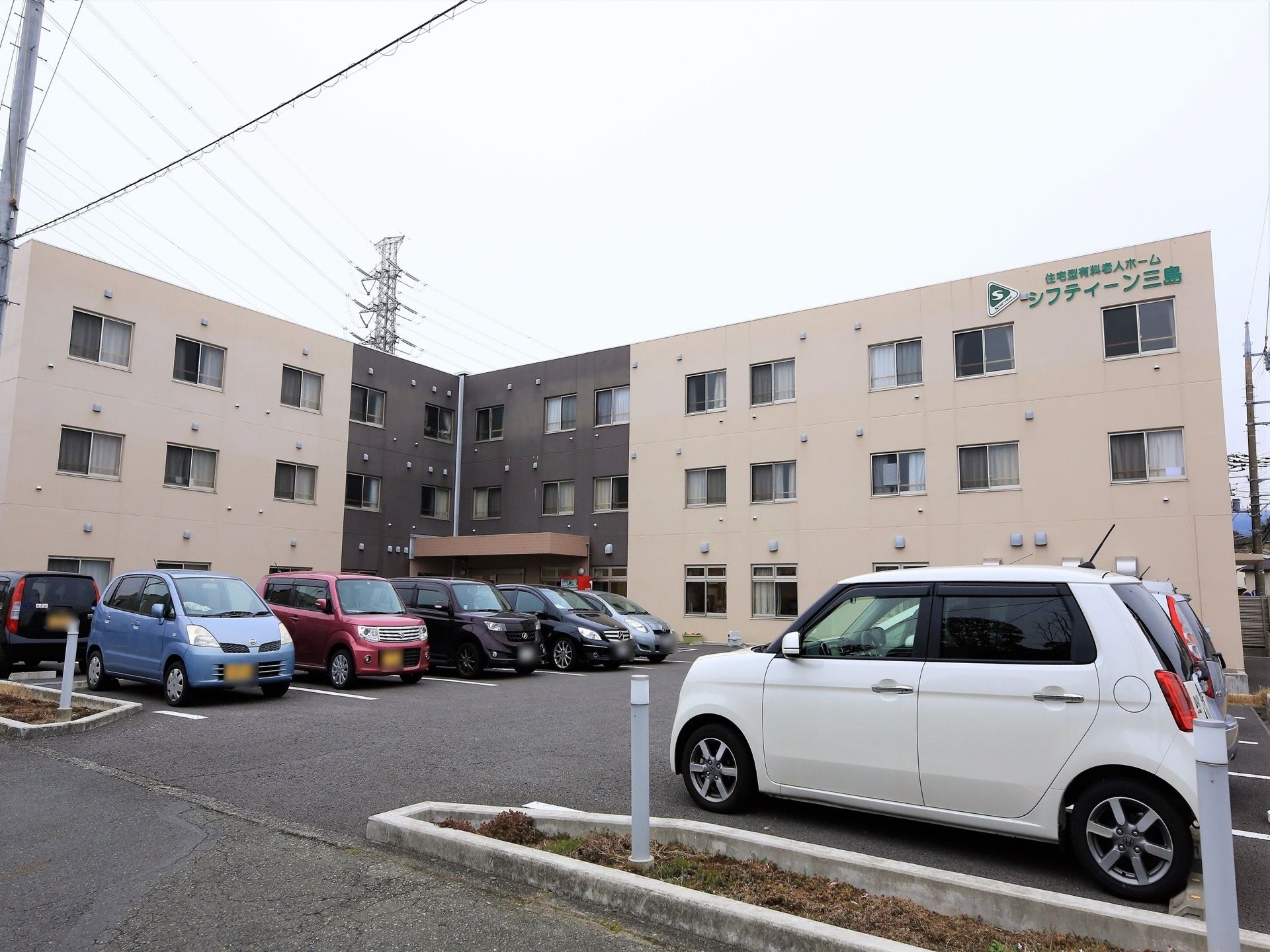 施設の外観は、ベージュとブラウンのツートンカラーである。建物の形はL字型である。敷地内に多数の駐車スペースがある。