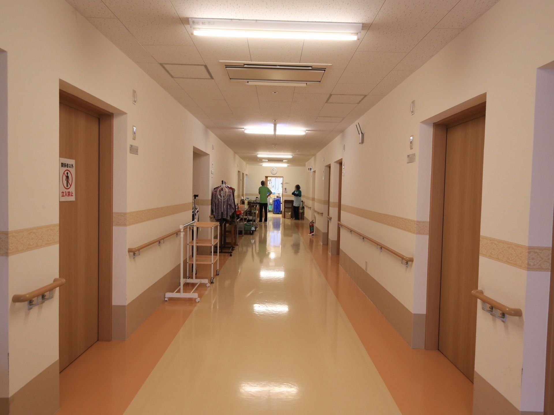 白い壁にベージュの床が伸び、両側の壁面に手すりが配された廊下