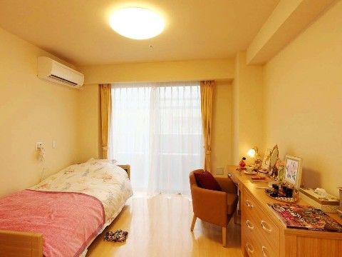 居室にはレースとカラーカーテンがかけられた窓がある。窓の近くにはベッド、テーブル、椅子、タンスが置かれている。