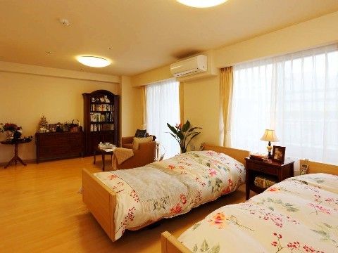 エアコンが設置された下側にはシングルベッドが2台並べられている。テーブルや椅子の近くには観葉植物が飾られている。