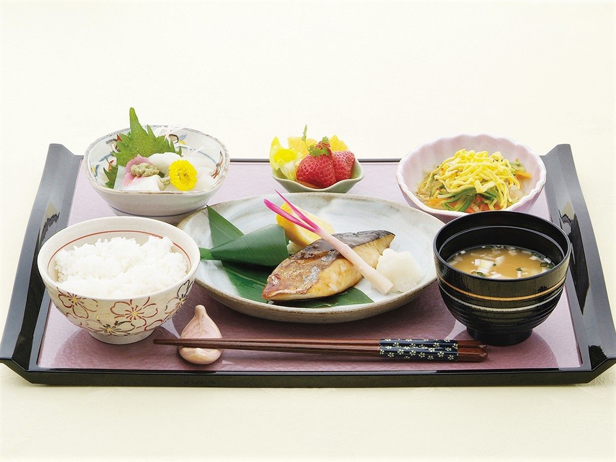 美しく盛り付けられた焼き魚をメインとした和食。ごはん、味噌汁、フルーツも添えられている。