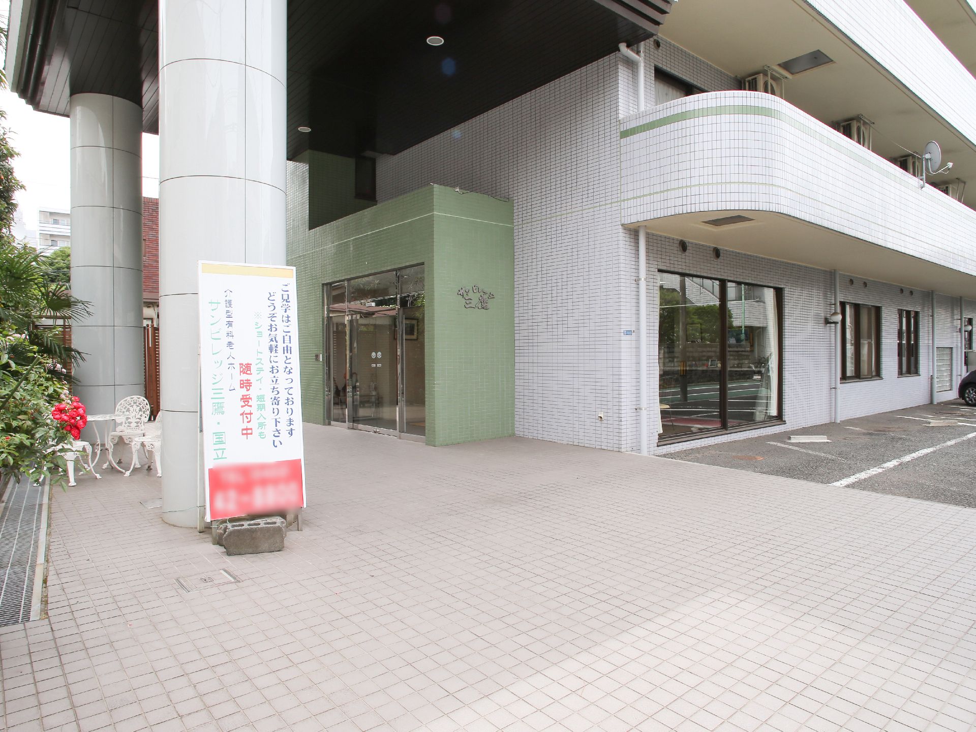 大型マンションのような造りで、太い柱が２本立った玄関ポーチになっている。入口前に見学案内の板が立てかけられている。