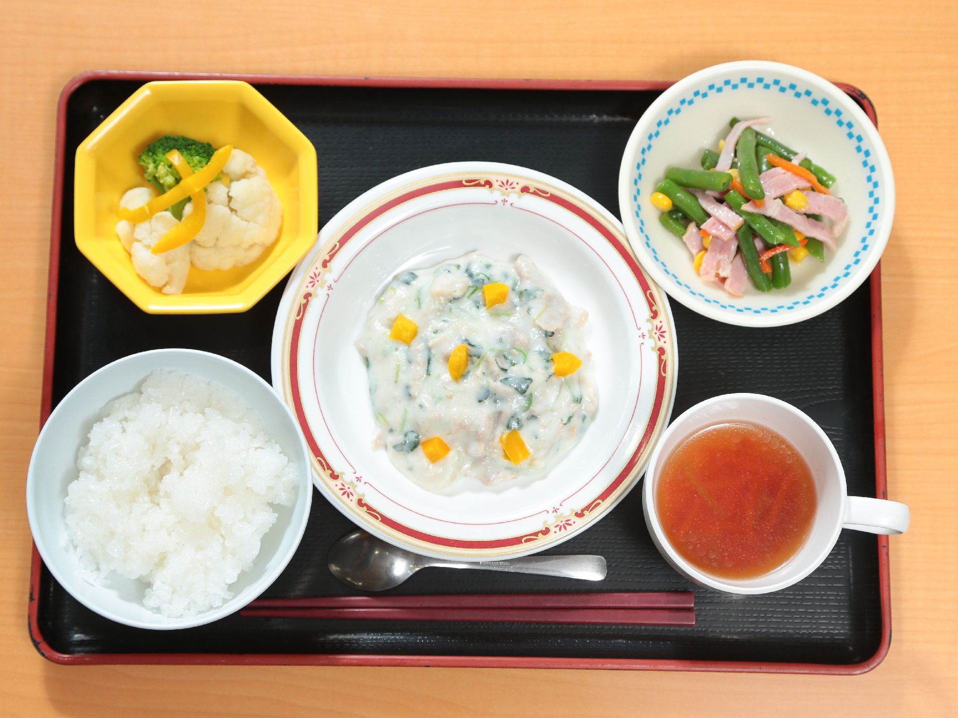 和風の黒いトレイに１人ずつ食事が配膳されている。白米とスープ、小鉢が２つあり、温野菜や和え物が並んでいる。