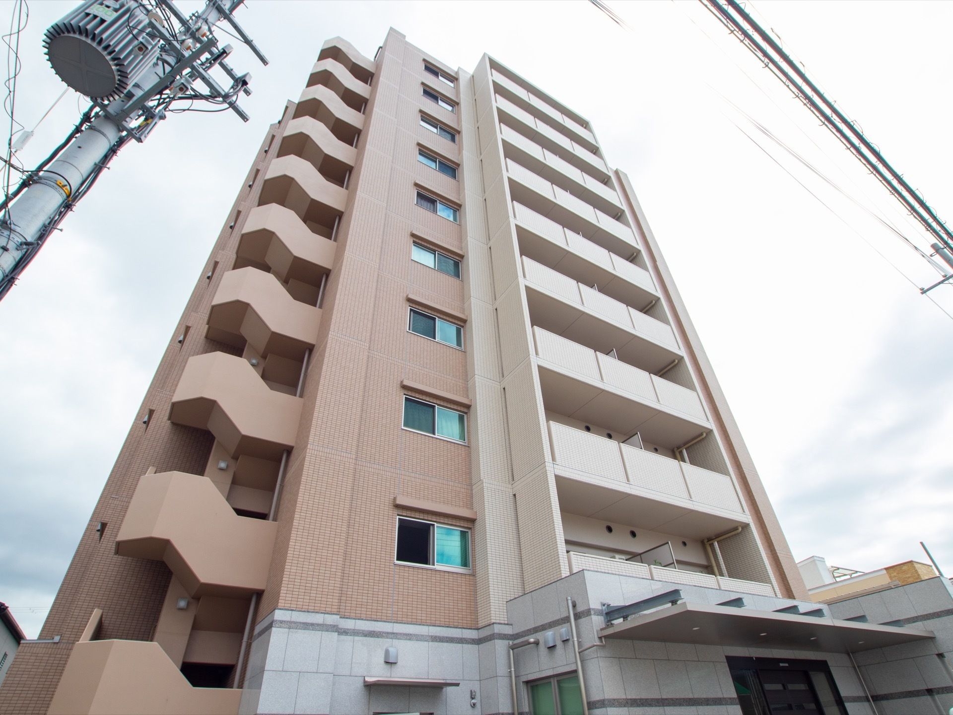 高層マンションのような外観で、１階に施設の入口があり、入口ドア前には屋根がついている。建物には外階段が設置されている。