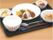 黒いトレーに、一人分の食事が用意されている。白米に小鉢、メインはハンバーグ、フルーツやスープもあり、栄養が考慮された食事メニューである。
