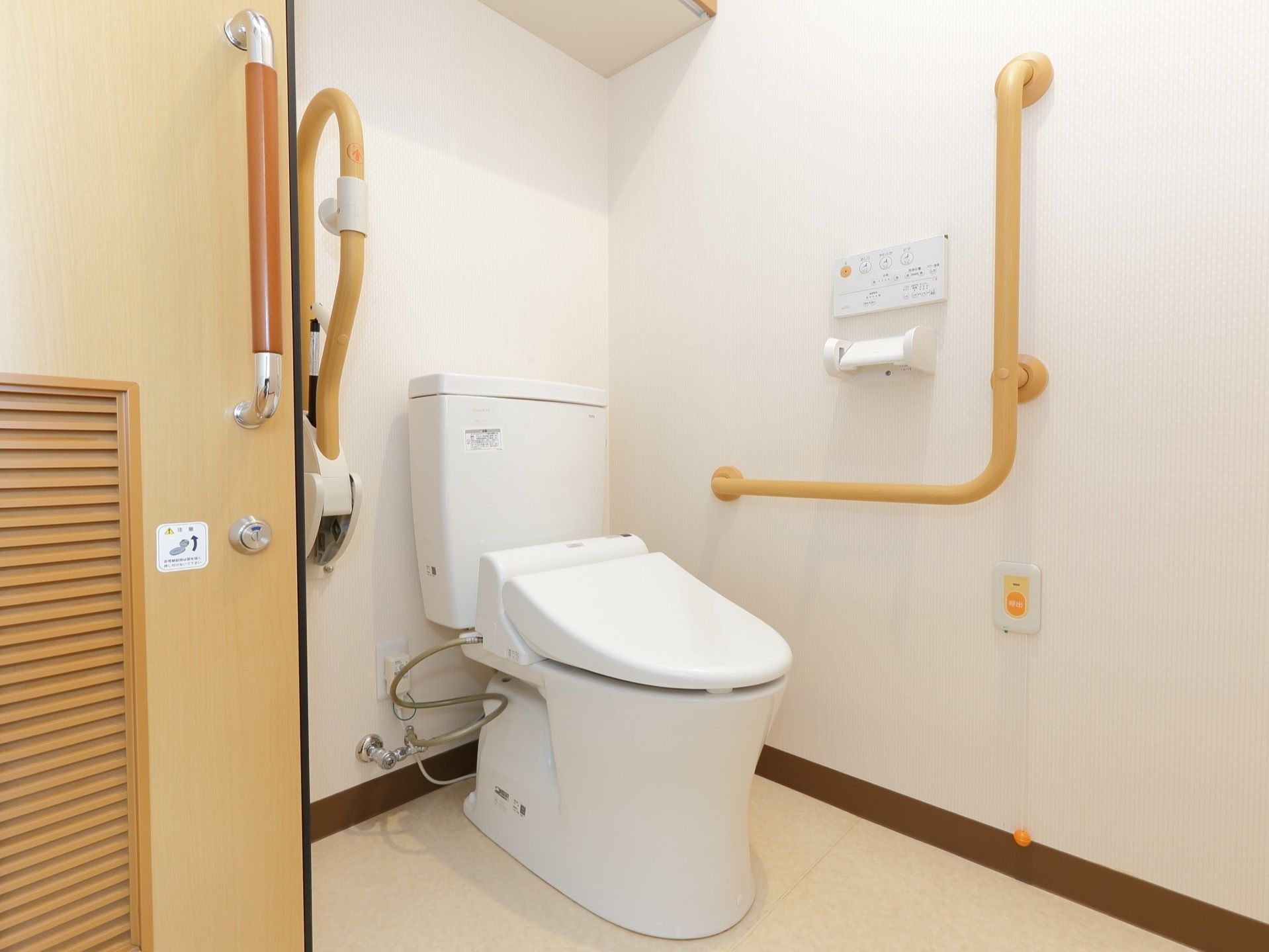 トイレにはフタの閉まった状態の便座があり、その両サイドには手すりが付けられている。壁にはナースコールも設置されている。