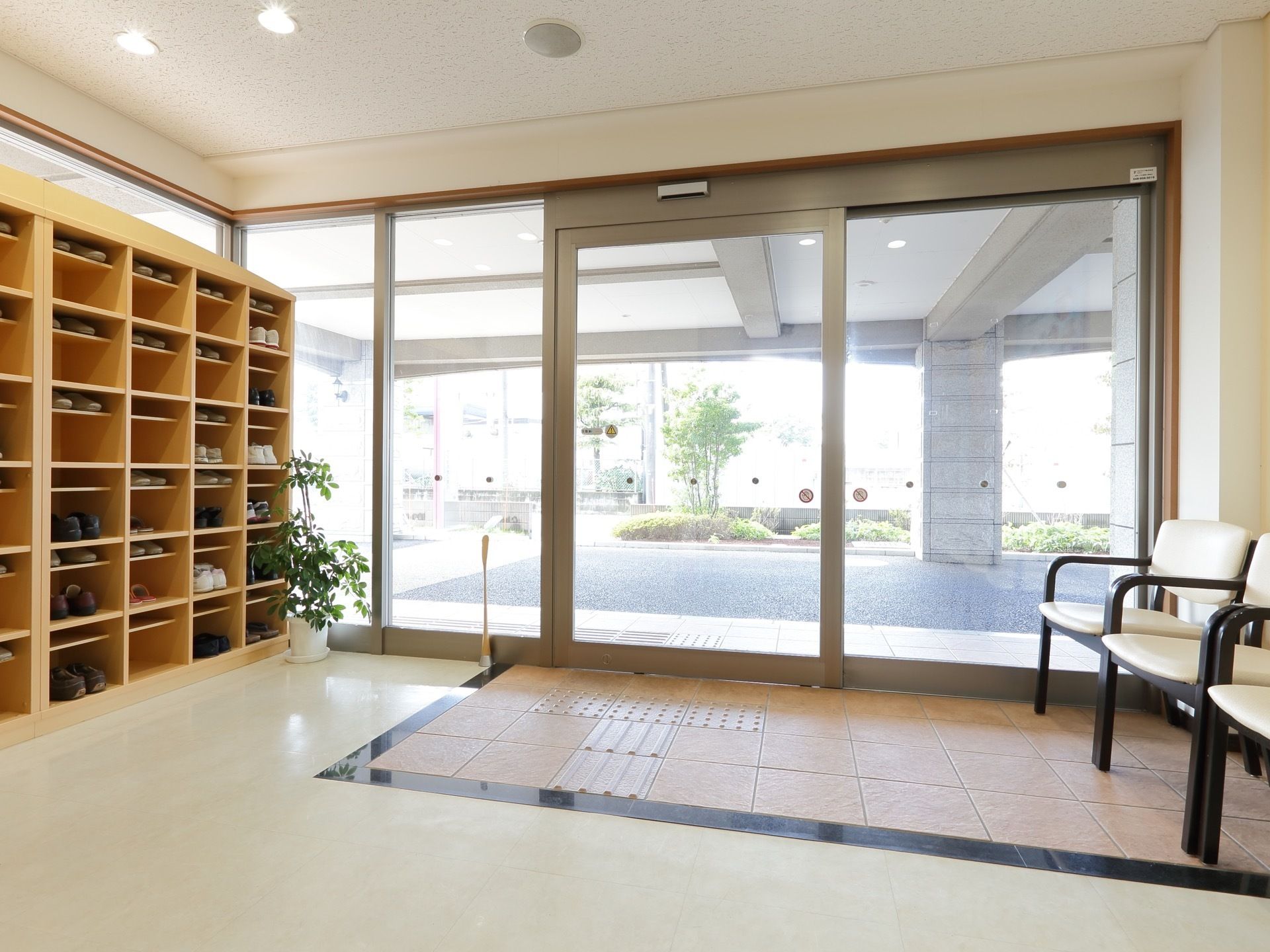 玄関には大きめの自動ドアがあり、その横にはイスが置かれている。壁際には、木製の靴箱が設置されている。