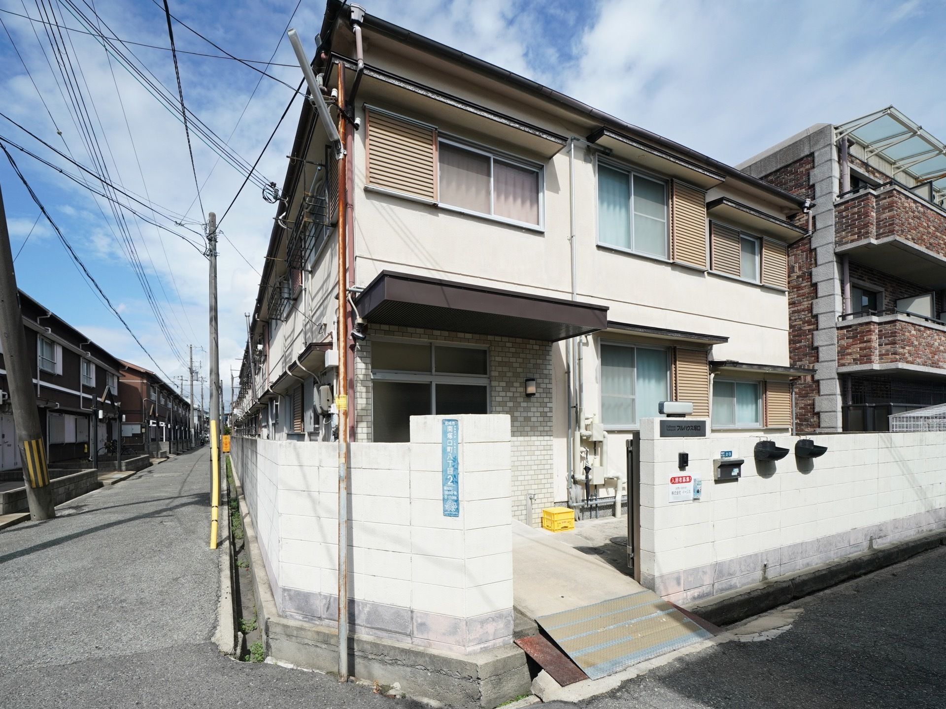 アパートのような外観をした施設建物。公道に接していて、周囲はコンクリートブロック製のフェンスでぐるりと囲われている。