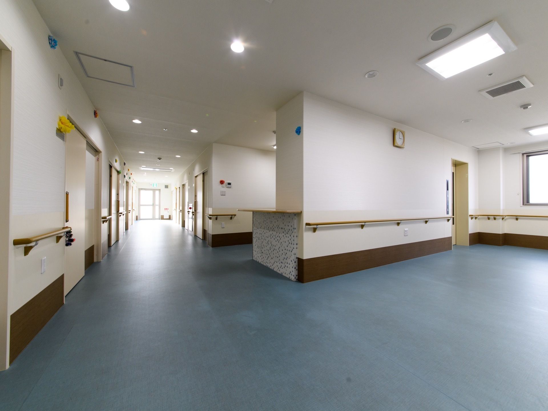 通路の幅は広い。手すりが両側に設置してある。エレベーターが完備されている。その横の壁に時計が掛けられている。