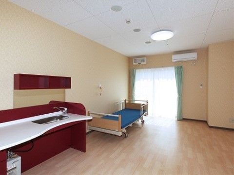 奥に窓がありその前にベッドが置かれ、さらに手前に洗面台があるフローリングの居室