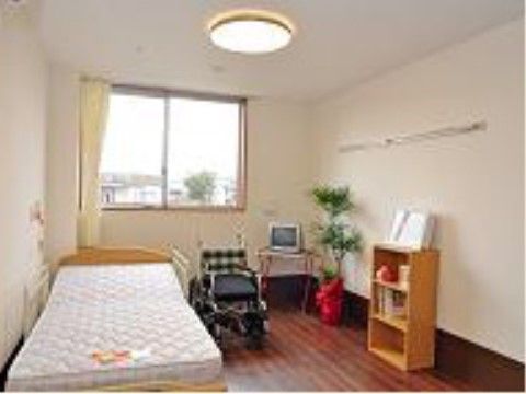 腰高窓から住宅街が見渡せる。低床型のベッド脇には非常用ブザーが付いている。小型のテレビと本棚がある。