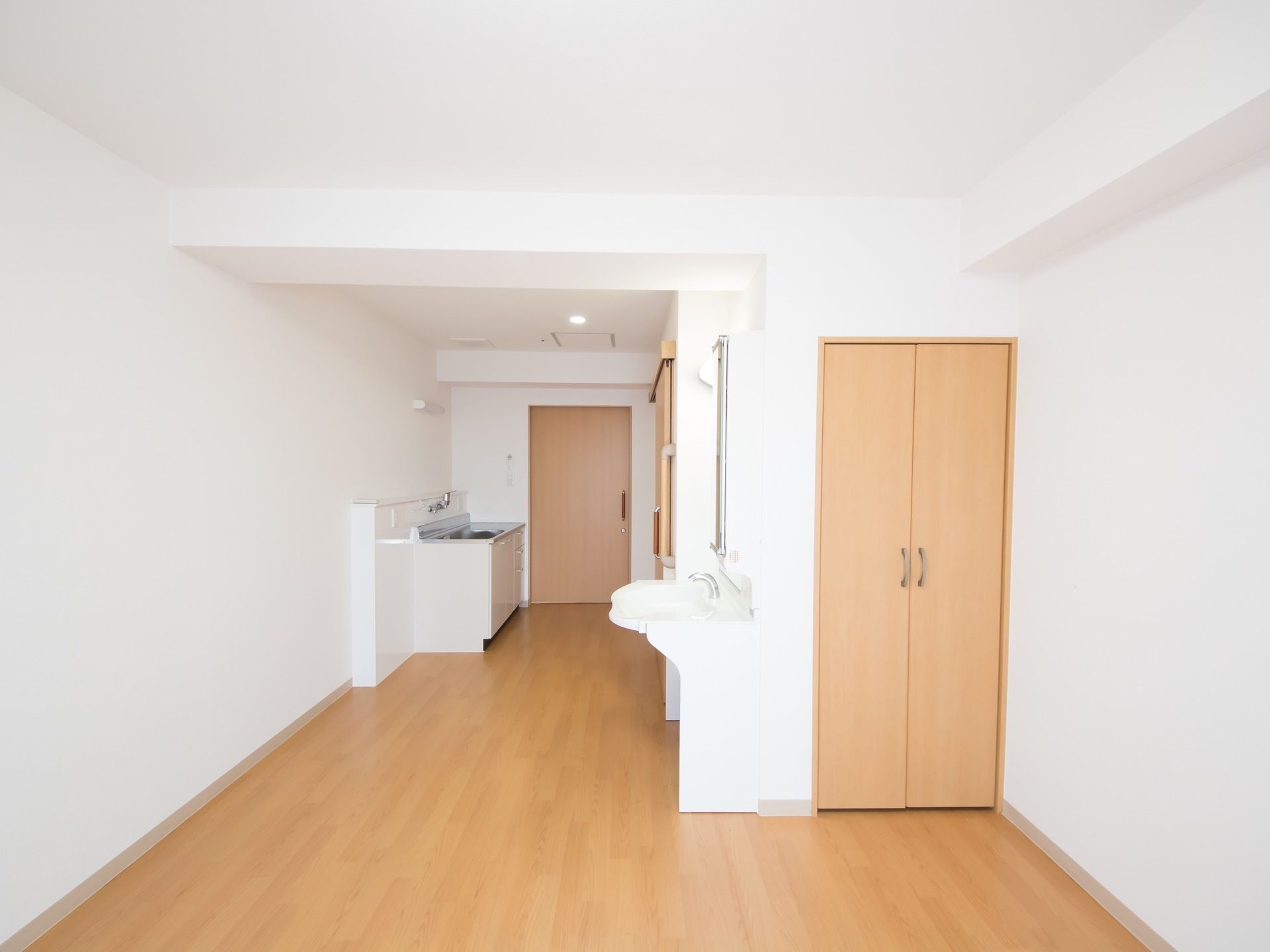 明るく縦長の居室空間。玄関扉脇にキッチン、トイレの近くに洗面台がある。備付の収納もある。足元はバリアフリー。