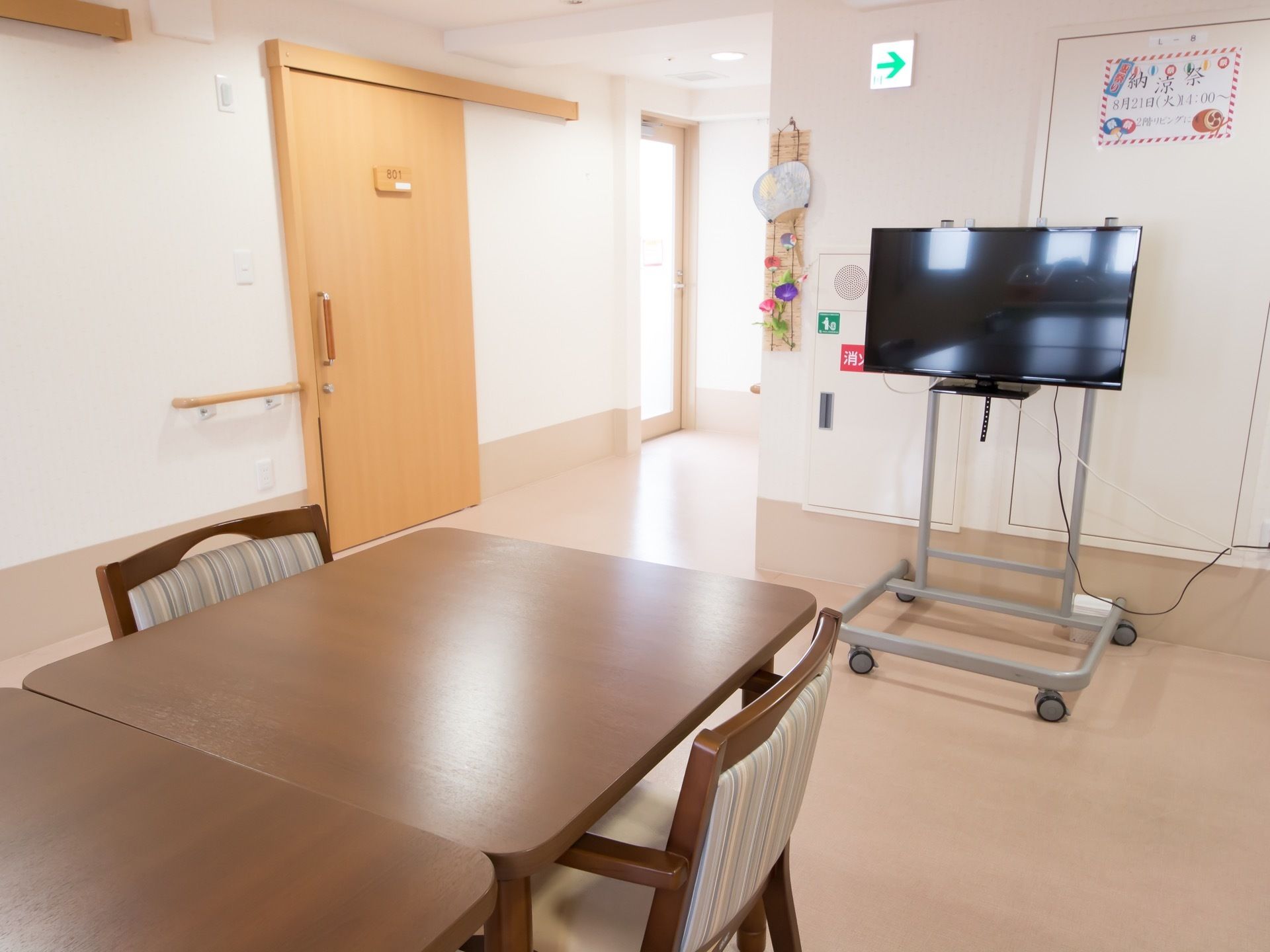木製のテーブルと椅子を配置している。大きい液晶テレビはキャスターがついたラックに設置している。床は凹凸のないフローリング。