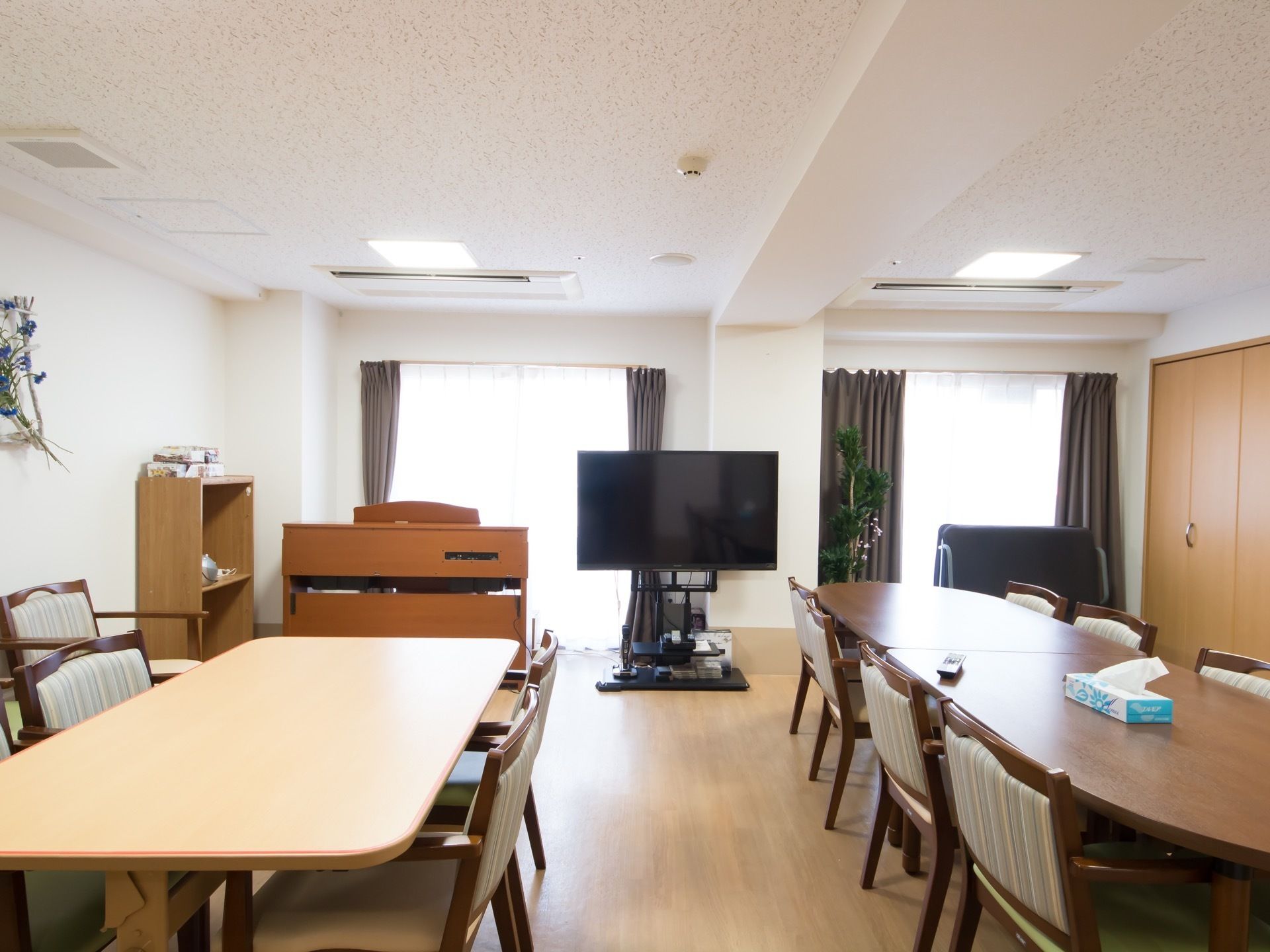 窓が多く室内を明るくしている。窓の前には大きなテレビが置かれている。天井にはエアコンがありいつでも快適な温度に保っている。