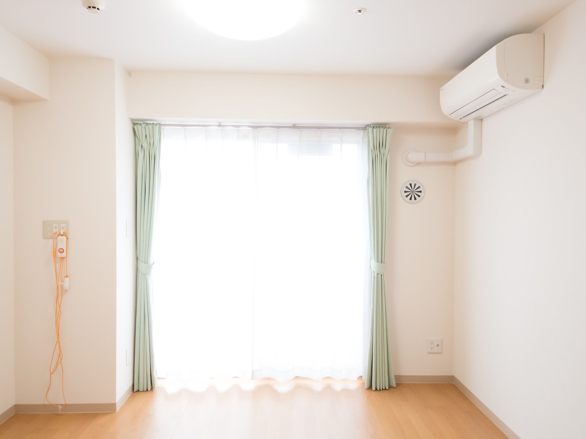 天井に丸型の大きなライトと火災報知器が設置されている。レースのかかった大きな窓があり、明るい日差しが差し込んでいる。