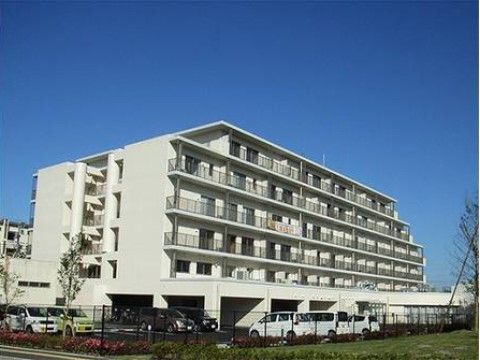 白い外壁の６階建ての建物。マンション風のしっかりとした造りである。アスファルトで舗装された駐車場があり、周囲にはツツジが植えられている。