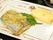 魚の煮物の上に細かく切って煮込まれたネギが乗っている。下に大葉が飾ってある。卵焼きも添えられている。