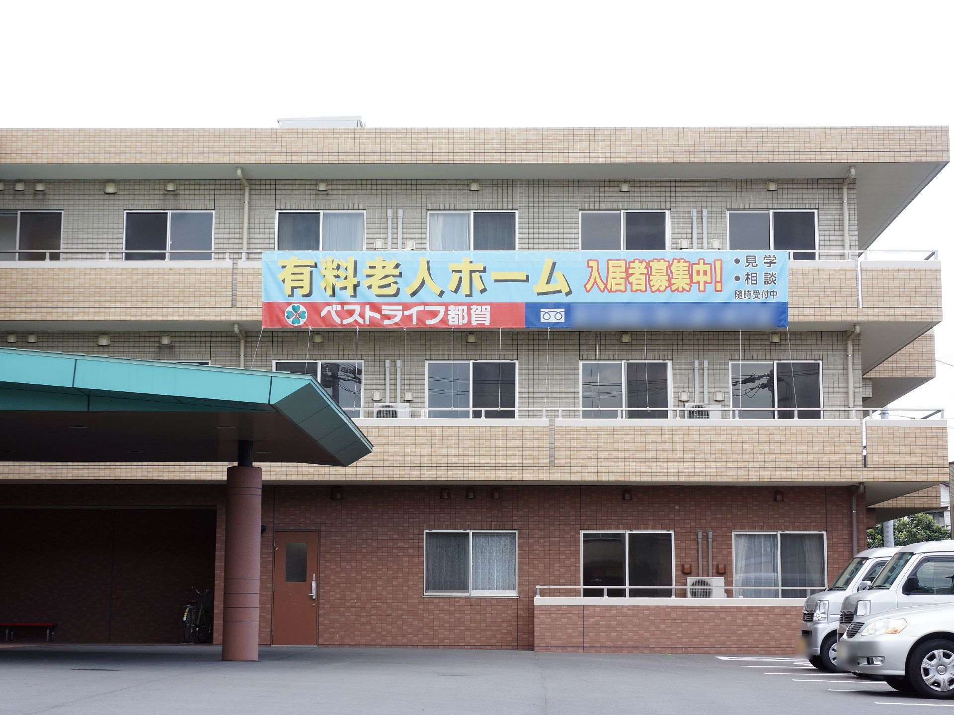 施設の建物は、レンガ風の造りになっている。玄関には天井屋根が付いていて、ベンチや車椅子が置かれている。入居者募集の掲示がされている。