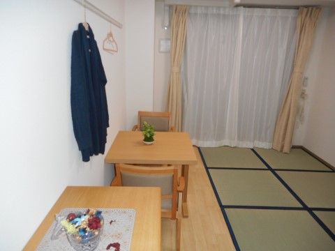 右側が畳敷き、左側が板間になっている部屋。板間部分に木製のサイドボードと座椅子のテーブルセットが置いてある。壁に服とハンガーがかかっている。