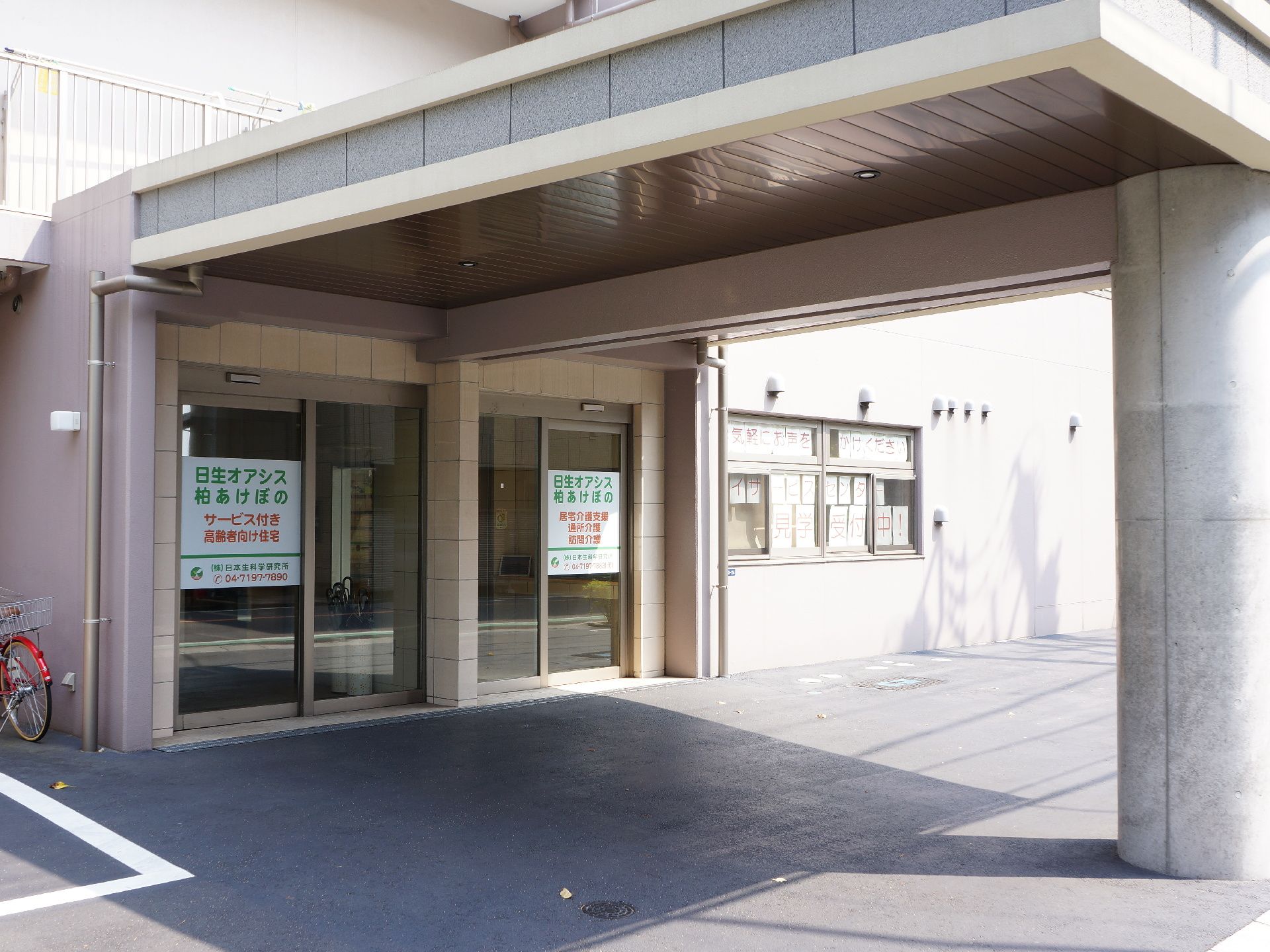 施設の玄関には2つの入り口ドアが設けられている。上部には大きな屋根があり、右側にある太くて丸い柱まで伸びている。