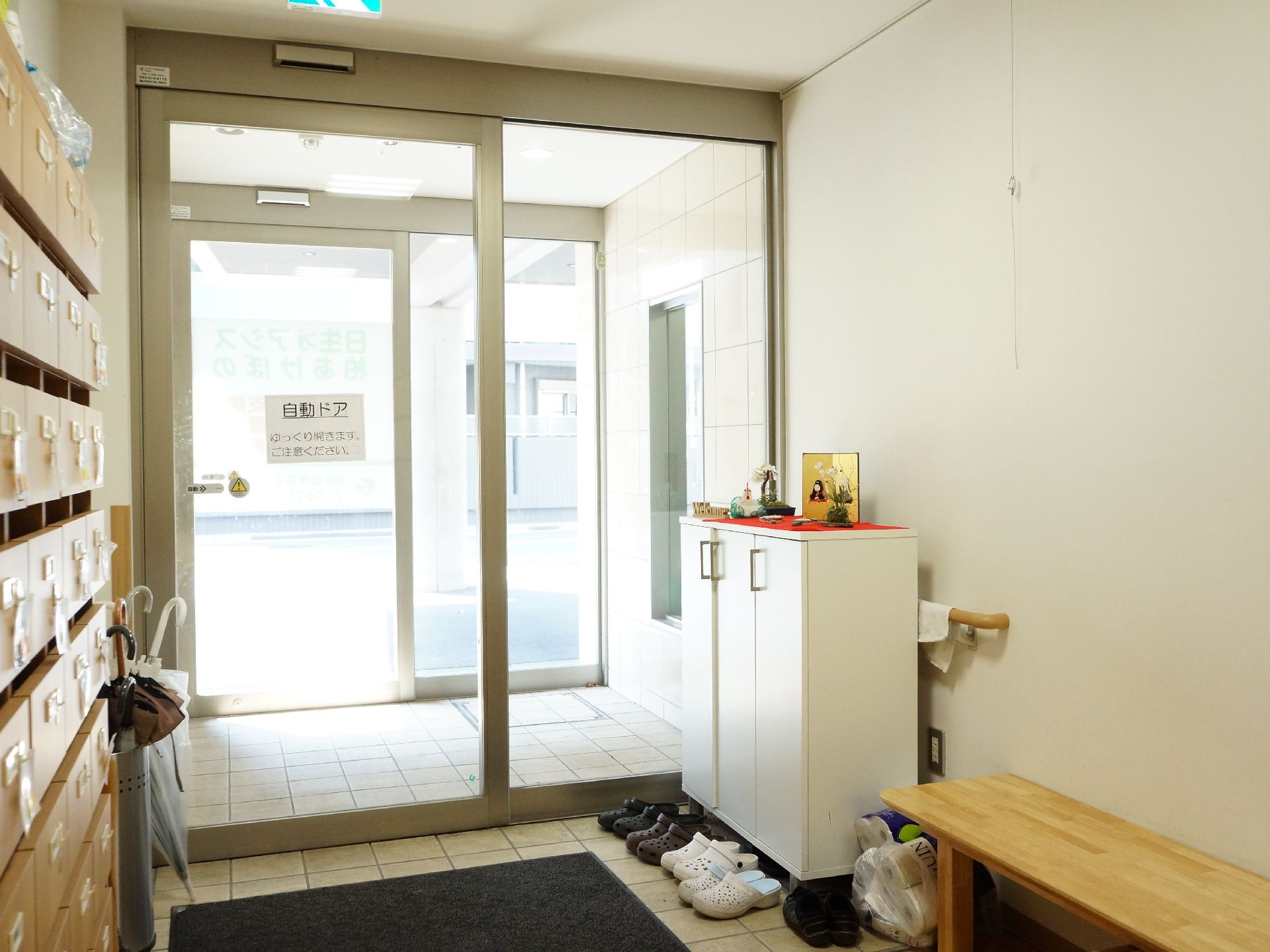 施設の玄関はガラス張りで、外の様子が見えるようになっている。ドアの内側には白いシューズボックスが置かれている。