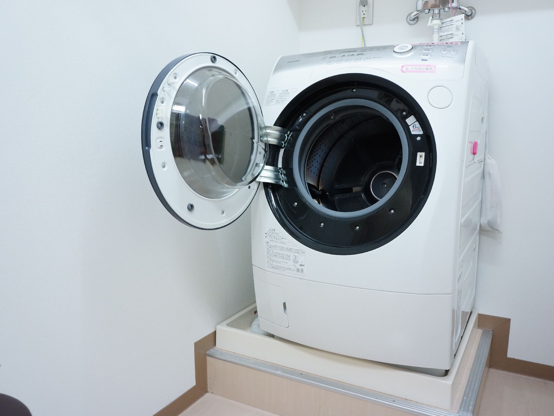 洗濯室の中にはドラム式の洗濯機が設置されている。上部の壁には専用の蛇口があり、左側にはコンセントが設けられている。