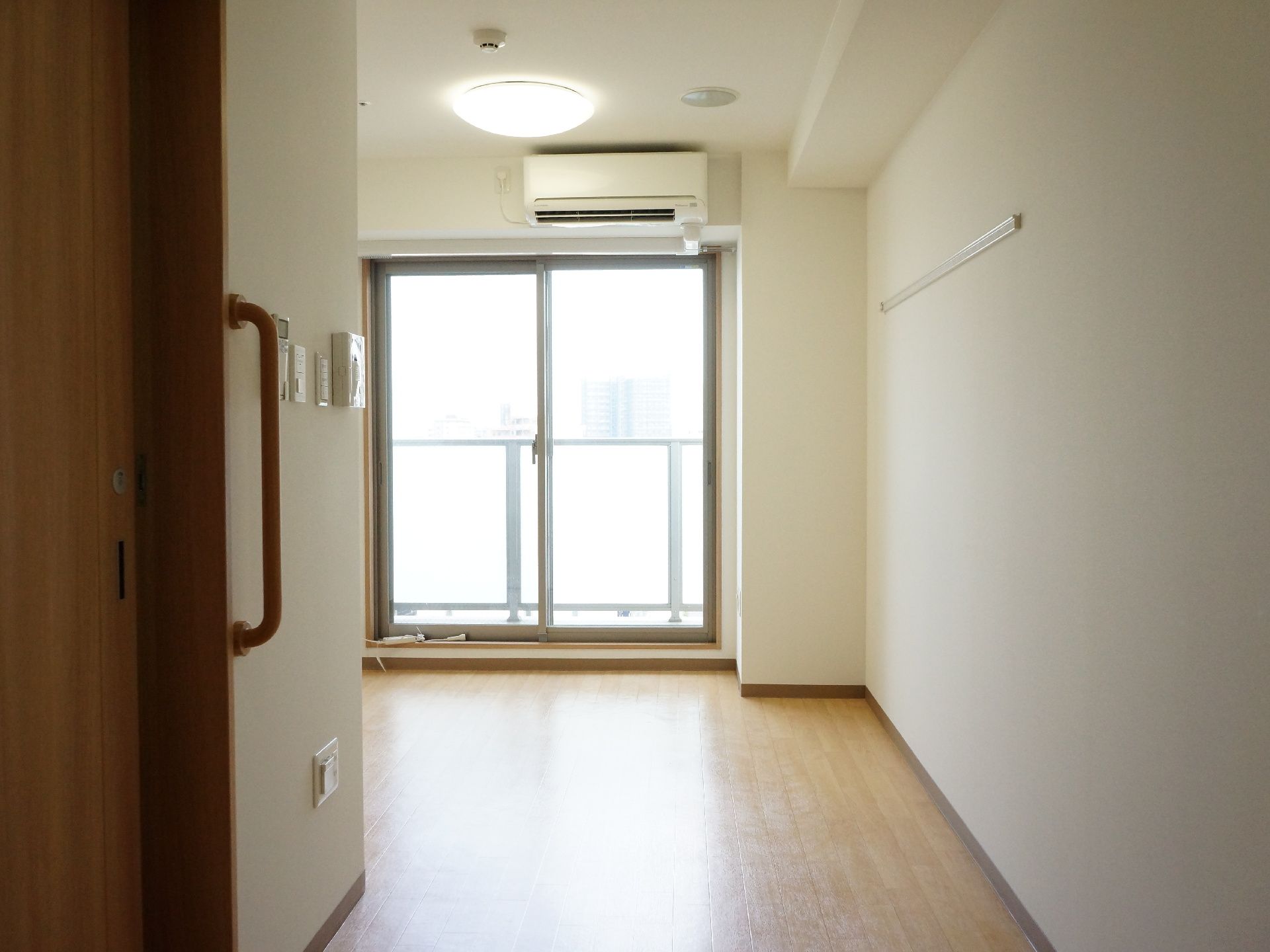 居室の床は全面フラットなフローリングである。左側の壁には手すりがあり、リモコンやスイッチ類が設置されている。