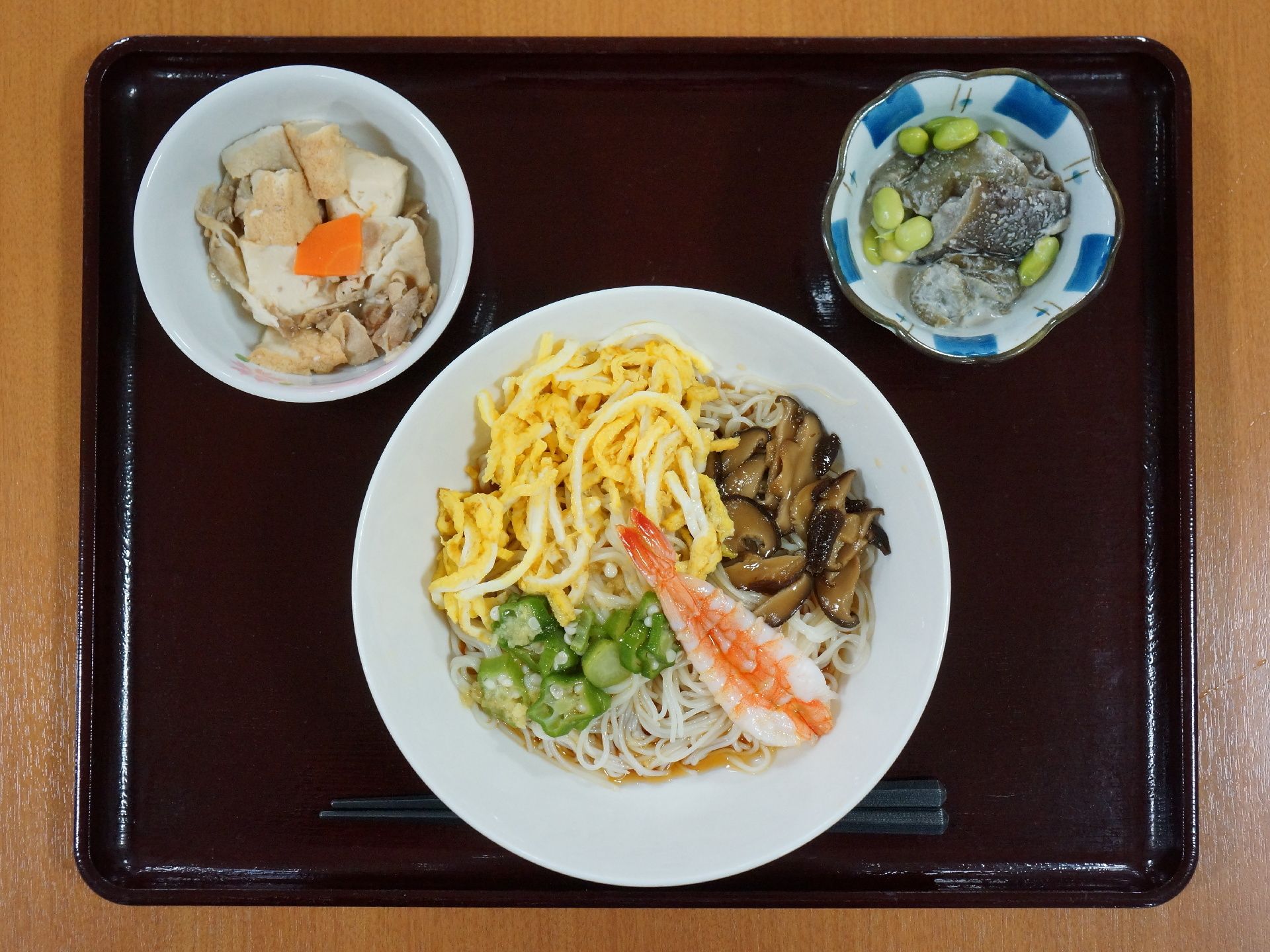 長方形のトレーの上に1人分の食事がセットされている。手前側に箸が置かれ、料理が盛られた器が3つ並べられている。