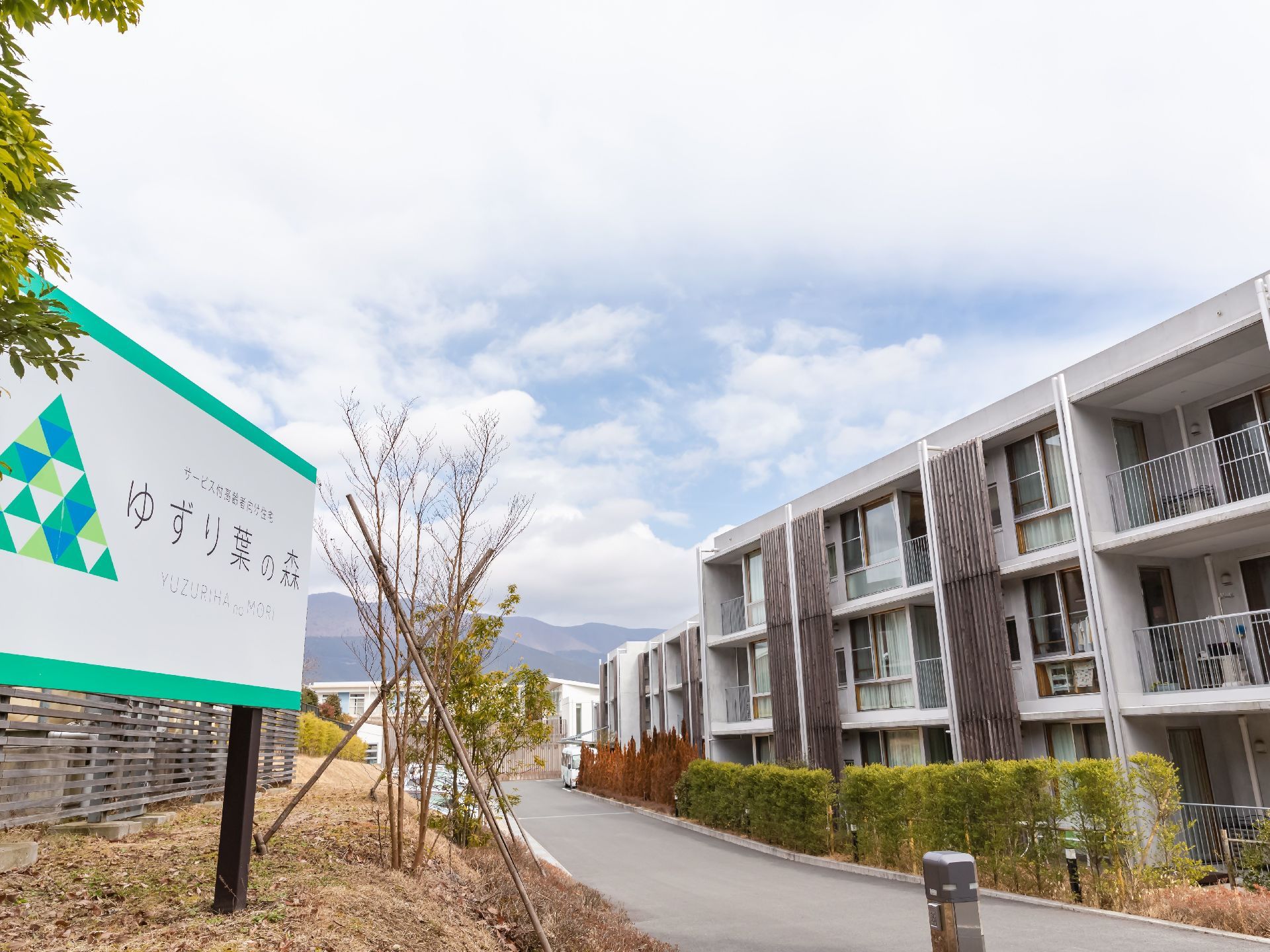 右手に３階建ての建物があり、奥に向かってカーブを描いて伸びている。左手前に大きな看板があり、施設名が書かれている。