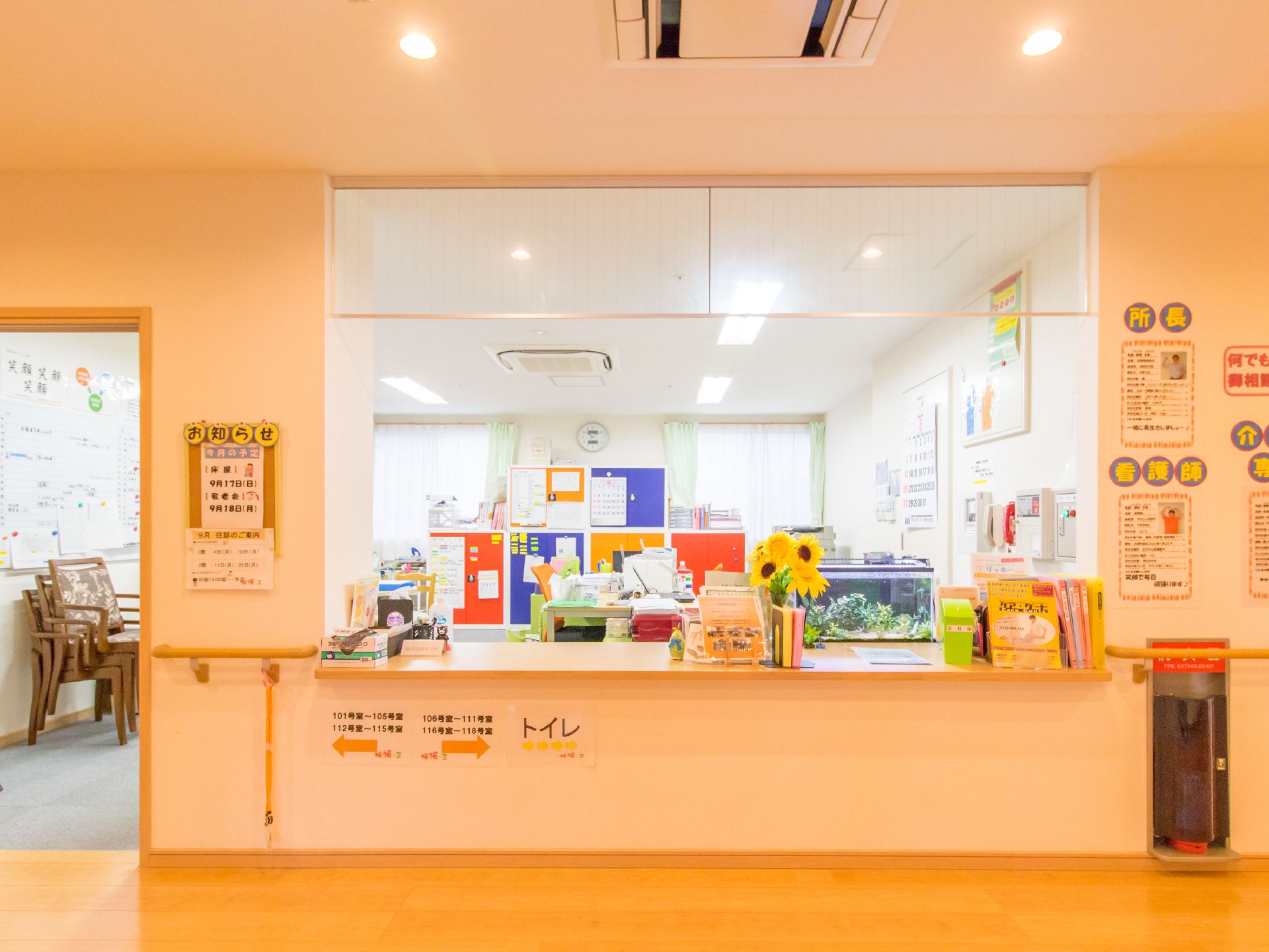 受付には花瓶に活けられた花があり、水槽も置いてある。受付の壁にはスタッフ紹介の紙が貼られており、手摺が設置されている。