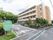 施設名を示す看板が設置されている。路面に一方通行と書かれている。建物の前に自動車が停車している。たくさんの植樹がされている。