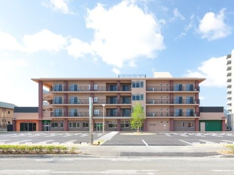 ベージュを基調とした4階建ての建物と手前に広がっている駐車場