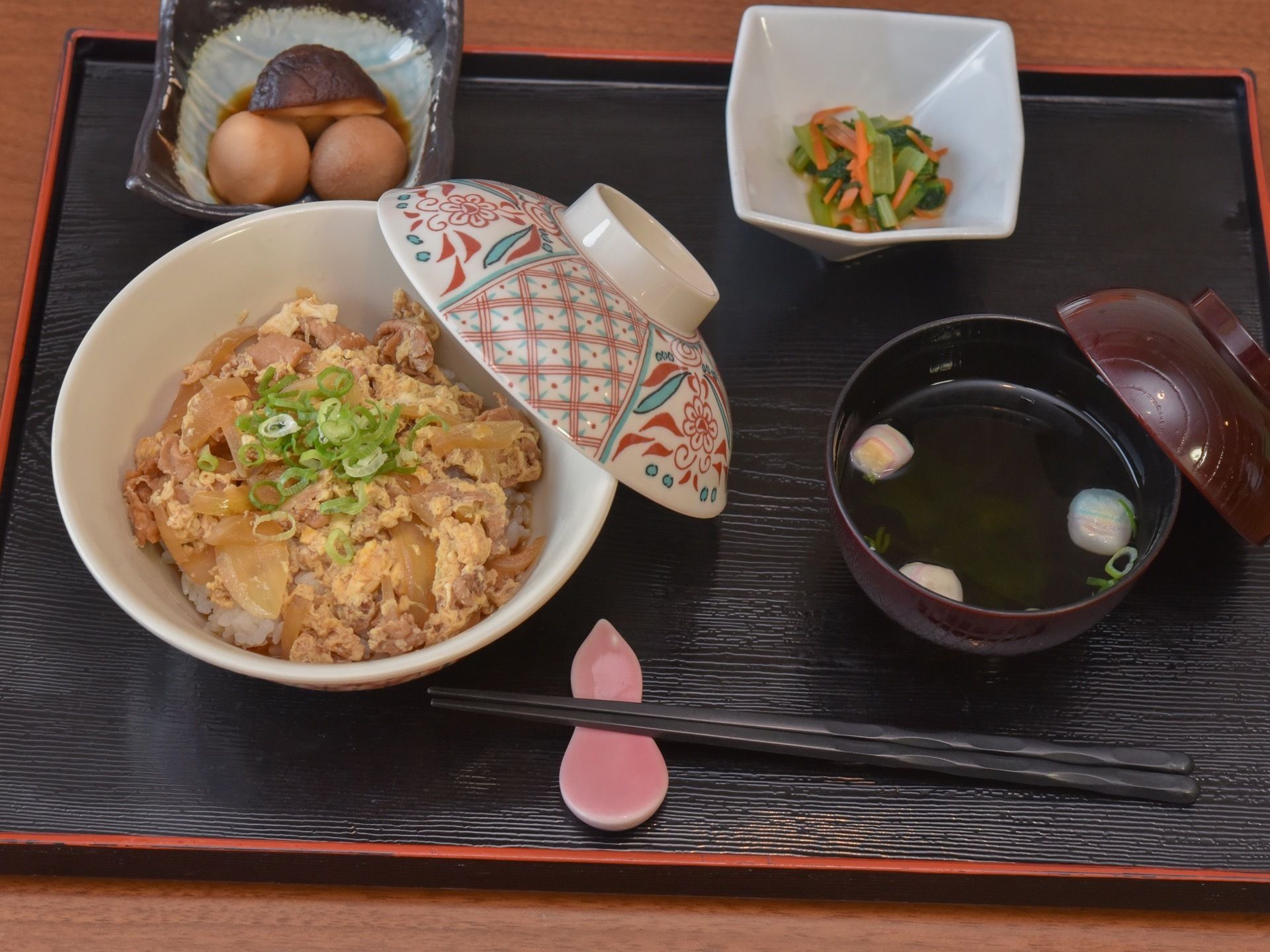 トレーの上に、食事が載っている。親子丼、吸い物、煮物、香の物のメニューである。箸置きが使われている。