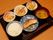 黒いトレーの上に、ごはん、漬物、焼き魚、味噌汁、副菜２品が並んでいる。茶色のお箸があり、持つ部分に凹凸がある。