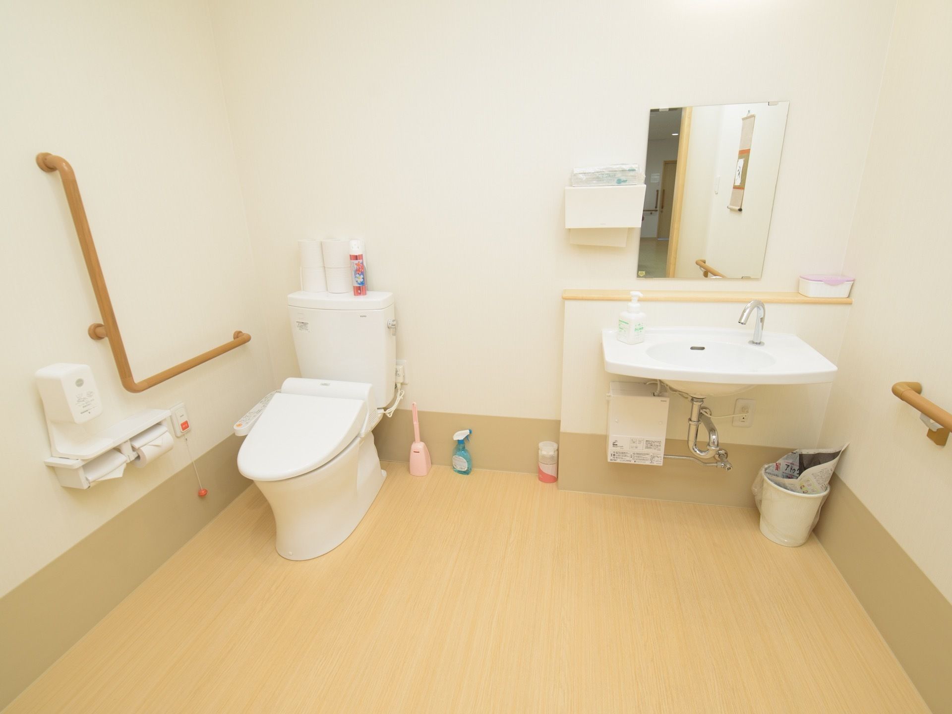 ゆとりのあるスペースに、洋式トイレと洗面台が配置してある。壁には手すりや呼び出しボタンが取り付けられている。