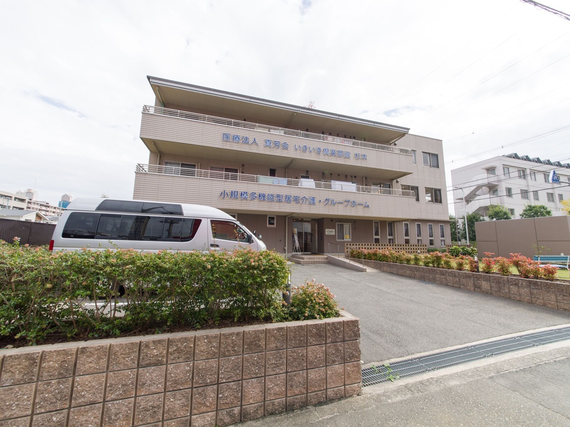 施設の前には大きな駐車場があり、木々を植えたスペースがある。建物は落ち着いたブラウンの外壁になっている。