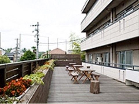 ウッドデッキに木のテーブルセットがいくつか設置されている。ブランターには手入れをされた草花が綺麗に咲いている。