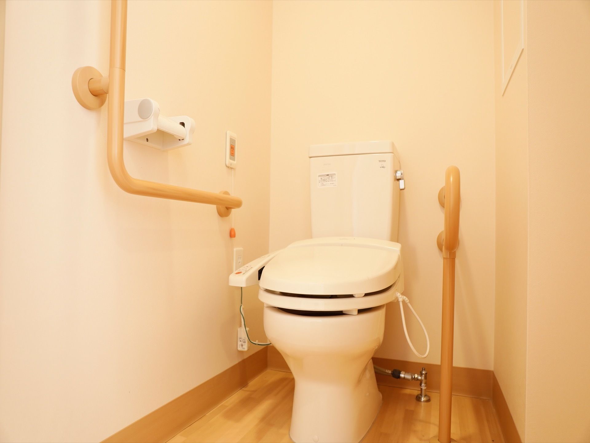 便器の両脇に手すりが設置されたトイレになっている。温水洗浄便座になっていて、緊急時ボタンが壁に設置されていて押しやすい。