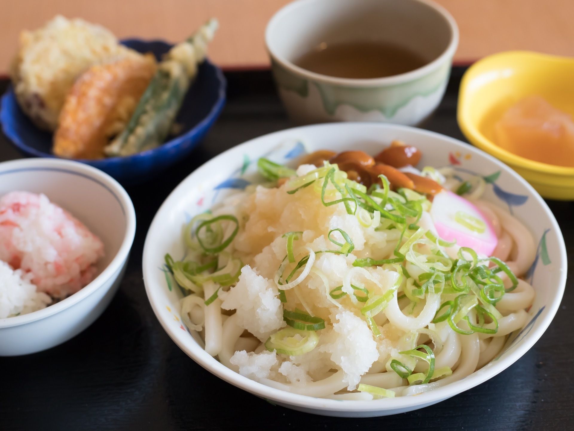 天ぷらとうどん。飲み物はお茶で、高齢者の方でも食べやすい和食である。色合いにも気を配っており、五感で楽しむことができる。