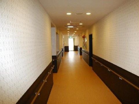 通路はまっすぐに続いている。壁紙には模様が入っている。長い手すりが取り付けられている。非常出口誘導灯が設置されている。