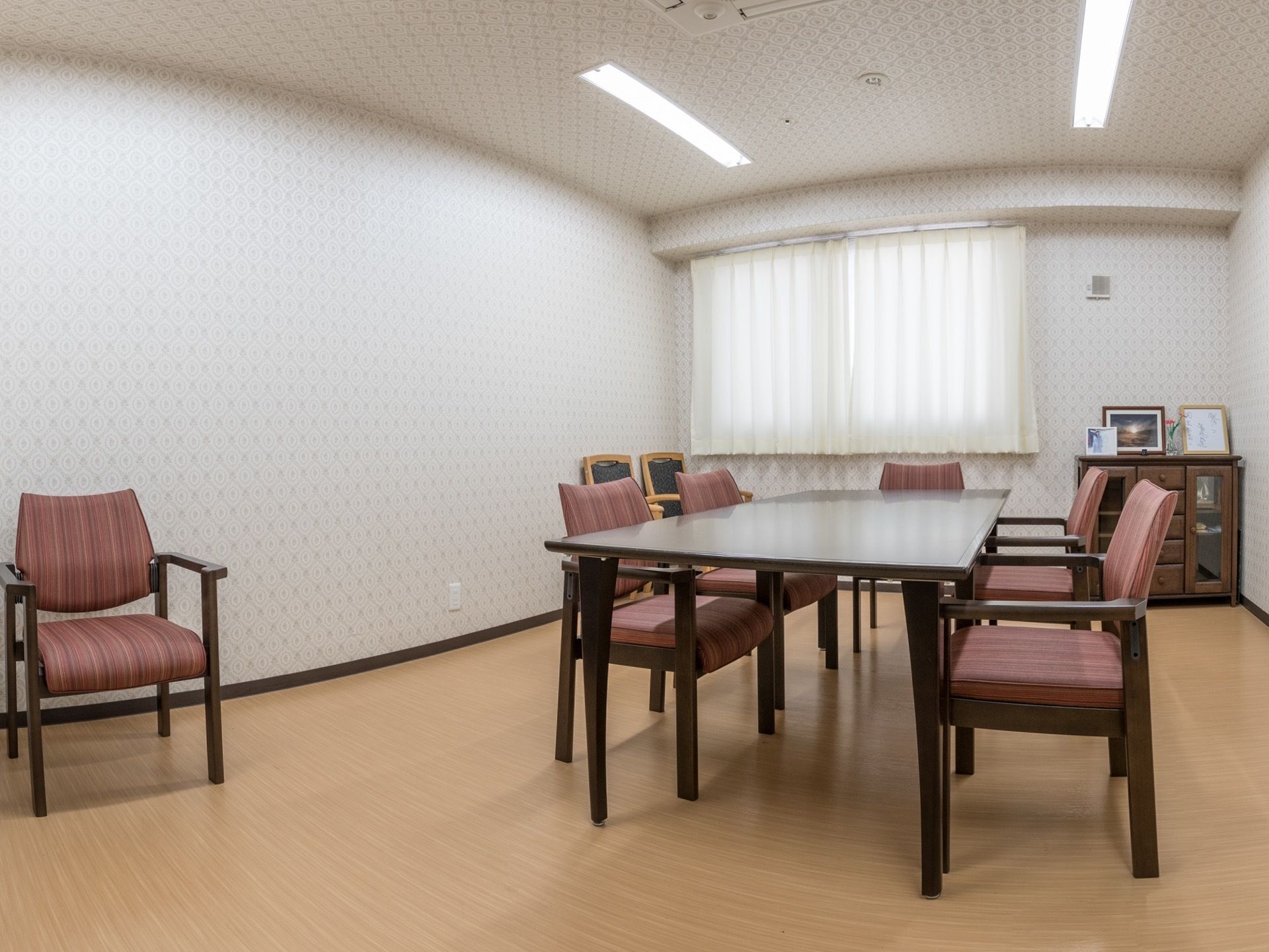 相談室の中央には、長テーブルと椅子が5脚並べられている。右奥には、木目調の小さな収納棚が設置されている。