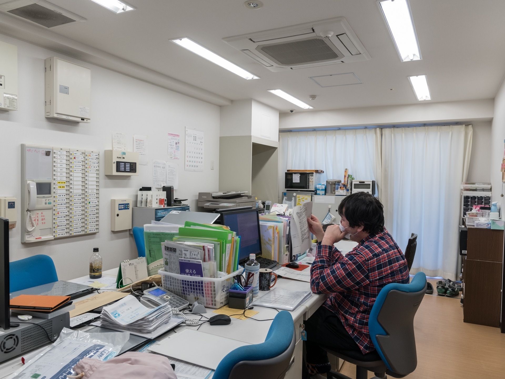 青い事務用いすに座って書類に手を伸ばすスタッフが中央にいる事務室