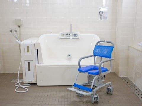 白い入浴介助用の器具が据えられ、青い車椅子の置かれた浴室