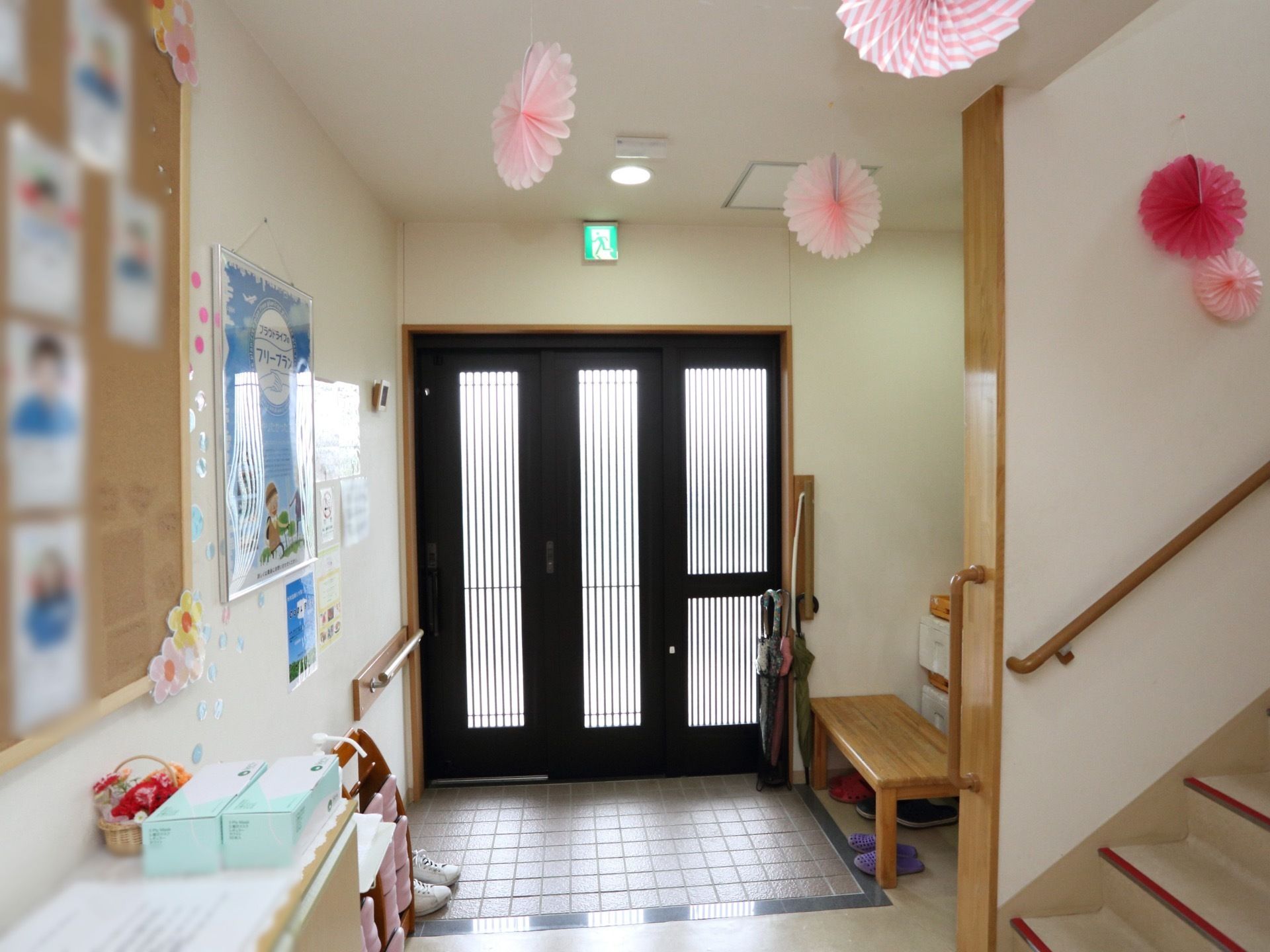 光が溢れる明るい玄関にベンチが備わっている。玄関横にはスタッフの顔写真が貼られており、壁や天井がピンクや赤の紙製品で飾り立てられている。