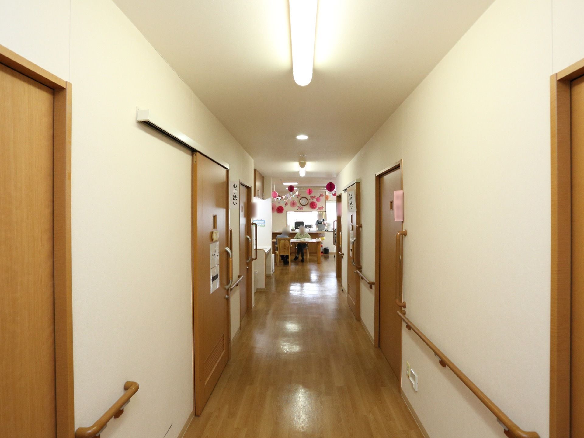 居室の扉が並ぶ廊下である。トイレの場所が分かりやすいように大きな文字で書かれた案内板が貼られている。