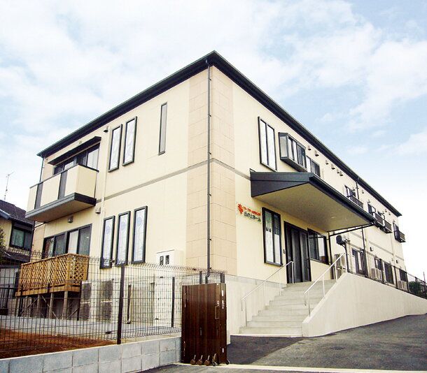 2階建ての建物で、玄関前には屋根を設置している。手すりのついた階段とスロープを設けており、隣には家庭菜園スペースがある。